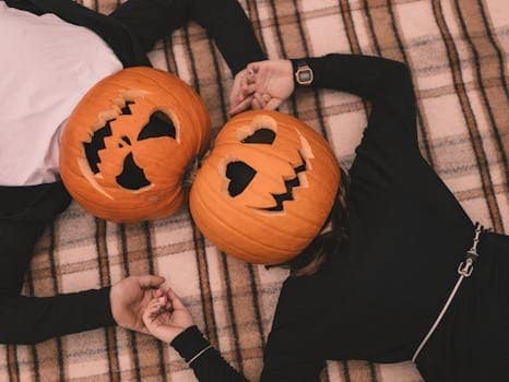 Two adults with pumpkin heads lying on a plaid blanket, symbolizing autumn festivity.