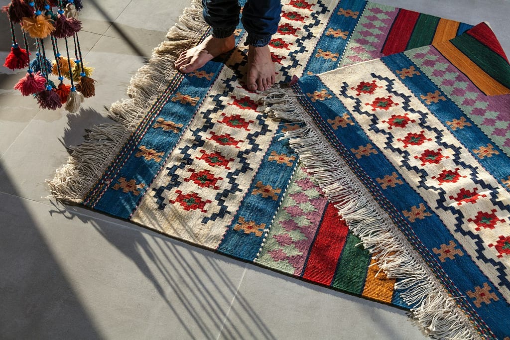 person in blue denim jeans standing on white blue and red area rug. living room.