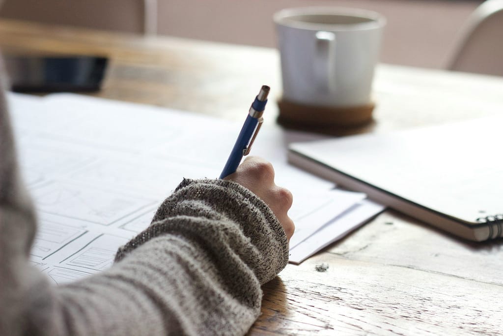 person writing on brown wooden table near white ceramic mug, TGPSC Group 2