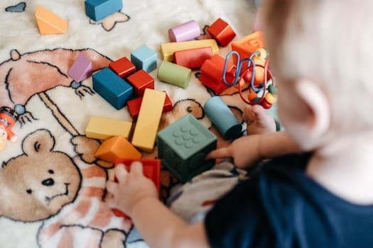 A toddler joyfully playing with a variety of colorful building blocks on a patterned blanket.