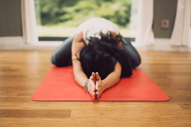 woman in white shirt lying on red mat on brown wooden table. top 10 Fitness Products