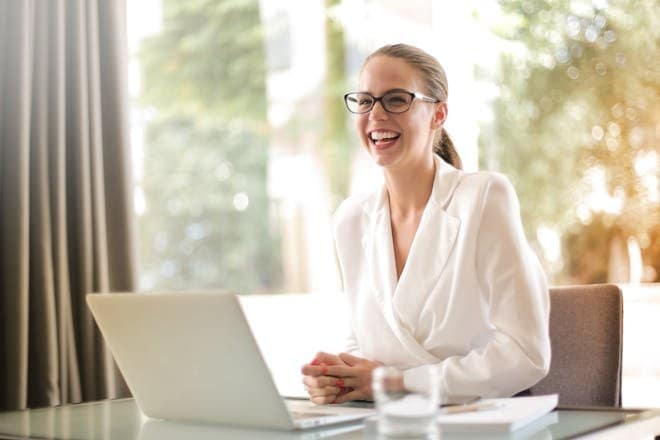 Cheerful businesswoman in glasses working on a laptop, in a bright and modern office setting. TEC Course