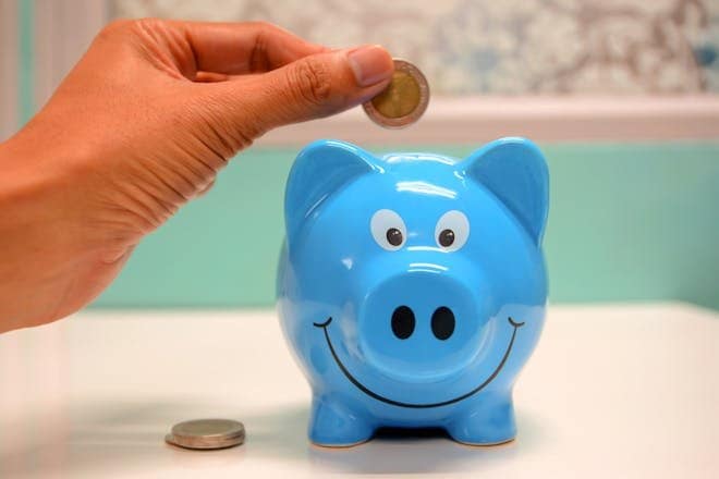 Hand inserting a coin into a blue piggy bank for savings and money management. India Post Payments Bank (IPPB) - Savings account offerings